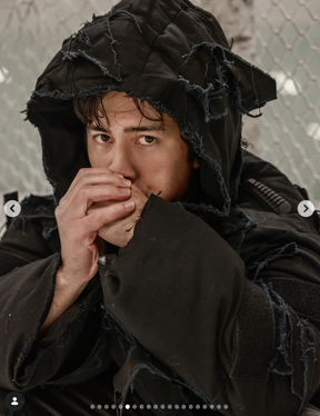 Person wearing a dark hooded outfit with a neutral background